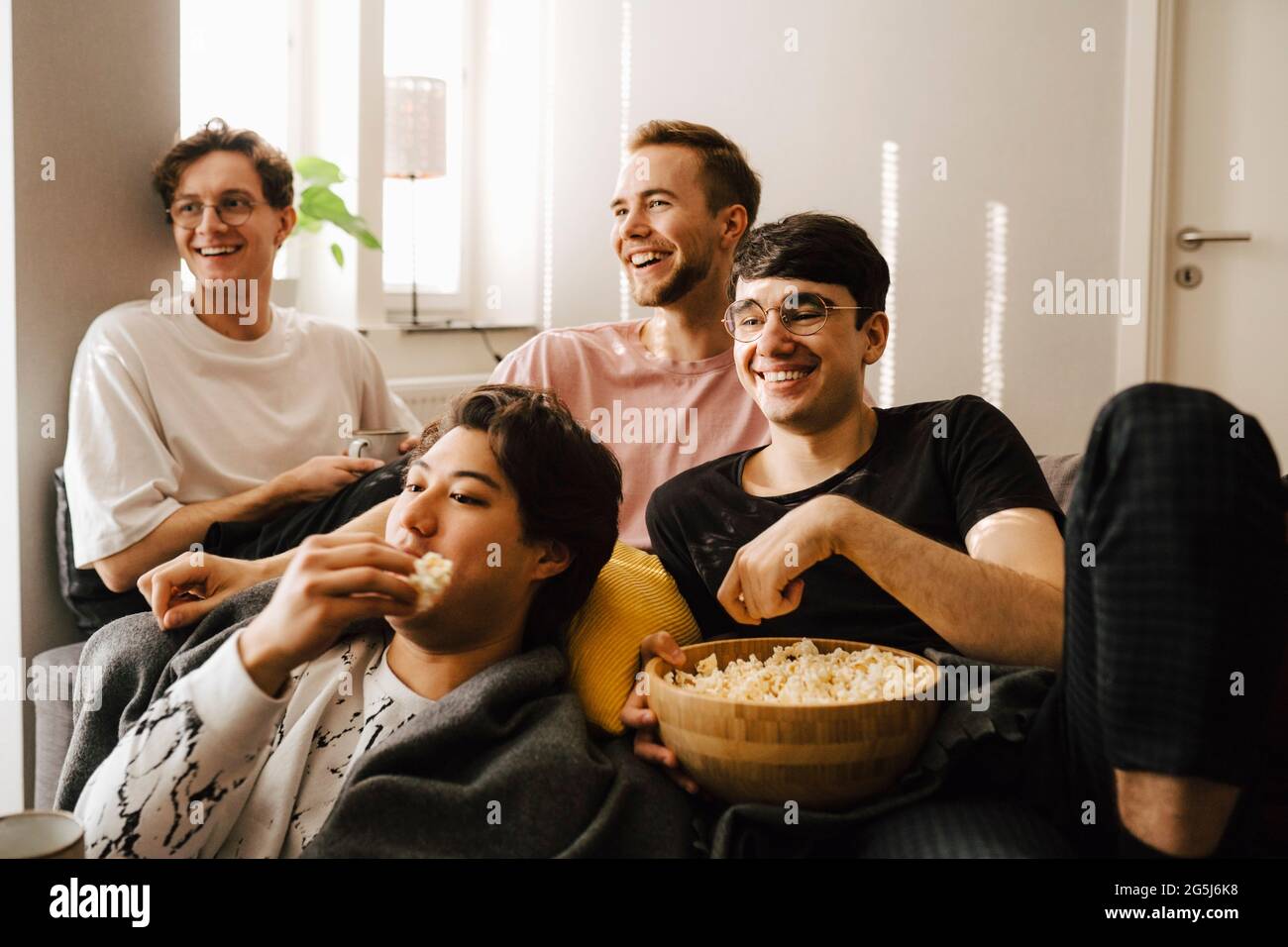 Des amis masculins souriants mangent du pop-corn tout en regardant des sports à la maison Banque D'Images