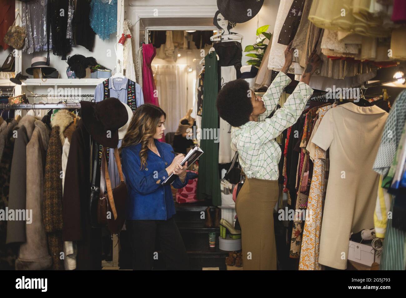 Une femme s'est mise à ranger ses vêtements dans un porte-vêtements pendant  que l'employé prend des notes au magasin Photo Stock - Alamy