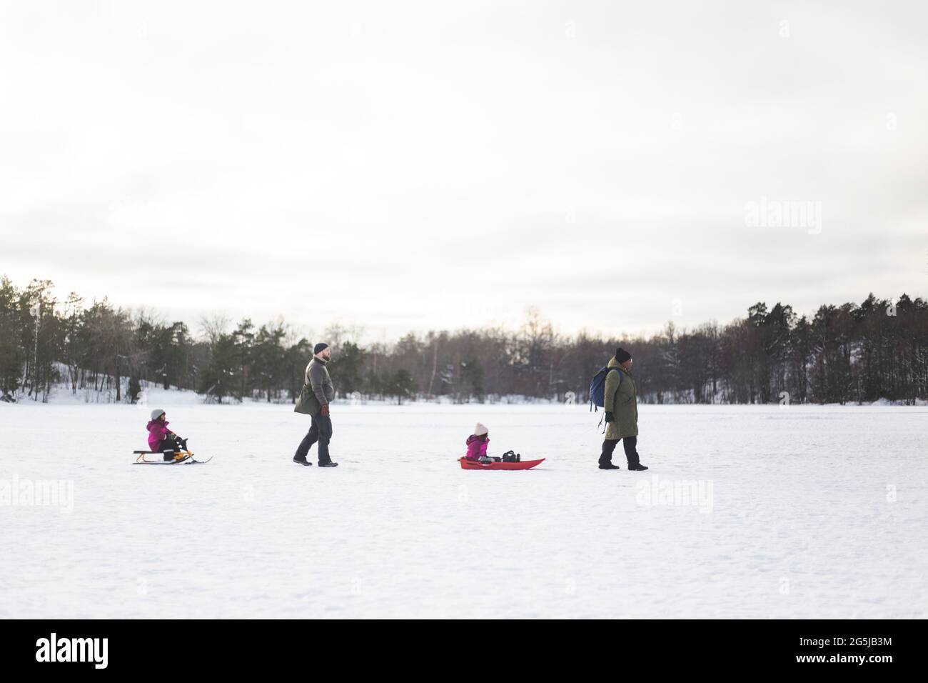 Les parents tirent leurs filles sur un toboggan et traînent pendant l'hiver Banque D'Images
