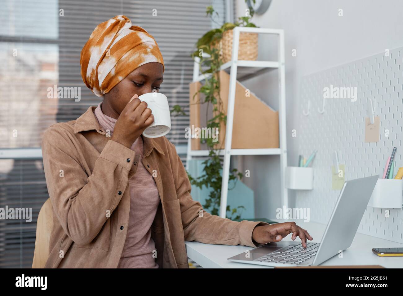 Portrait d'une femme afro-américaine moderne portant un foulard au bureau et utilisant un ordinateur portable, espace copie Banque D'Images
