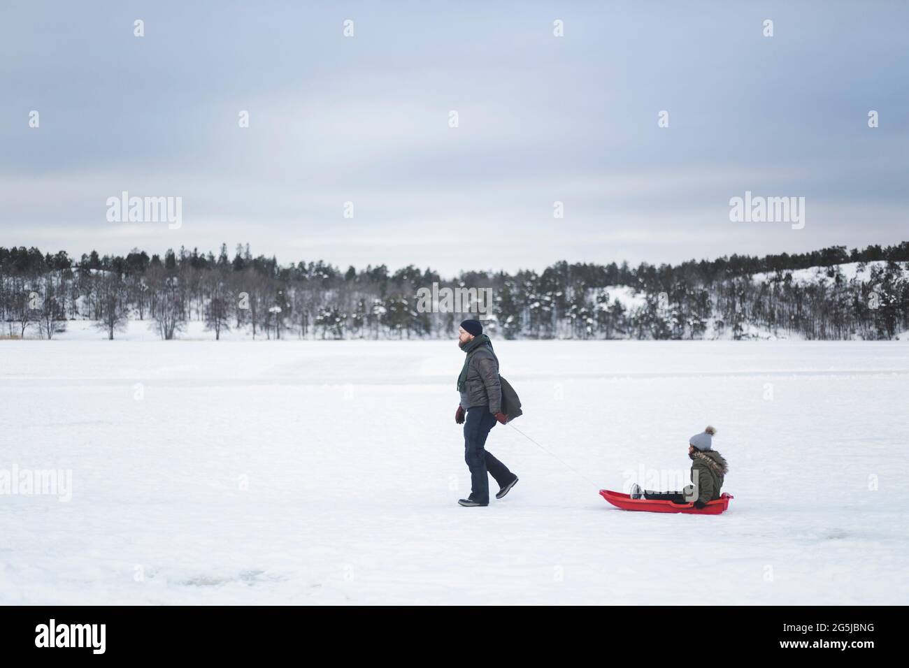 Le père tire sa fille assise sur un toboggan tout en marchant pendant l'hiver Banque D'Images