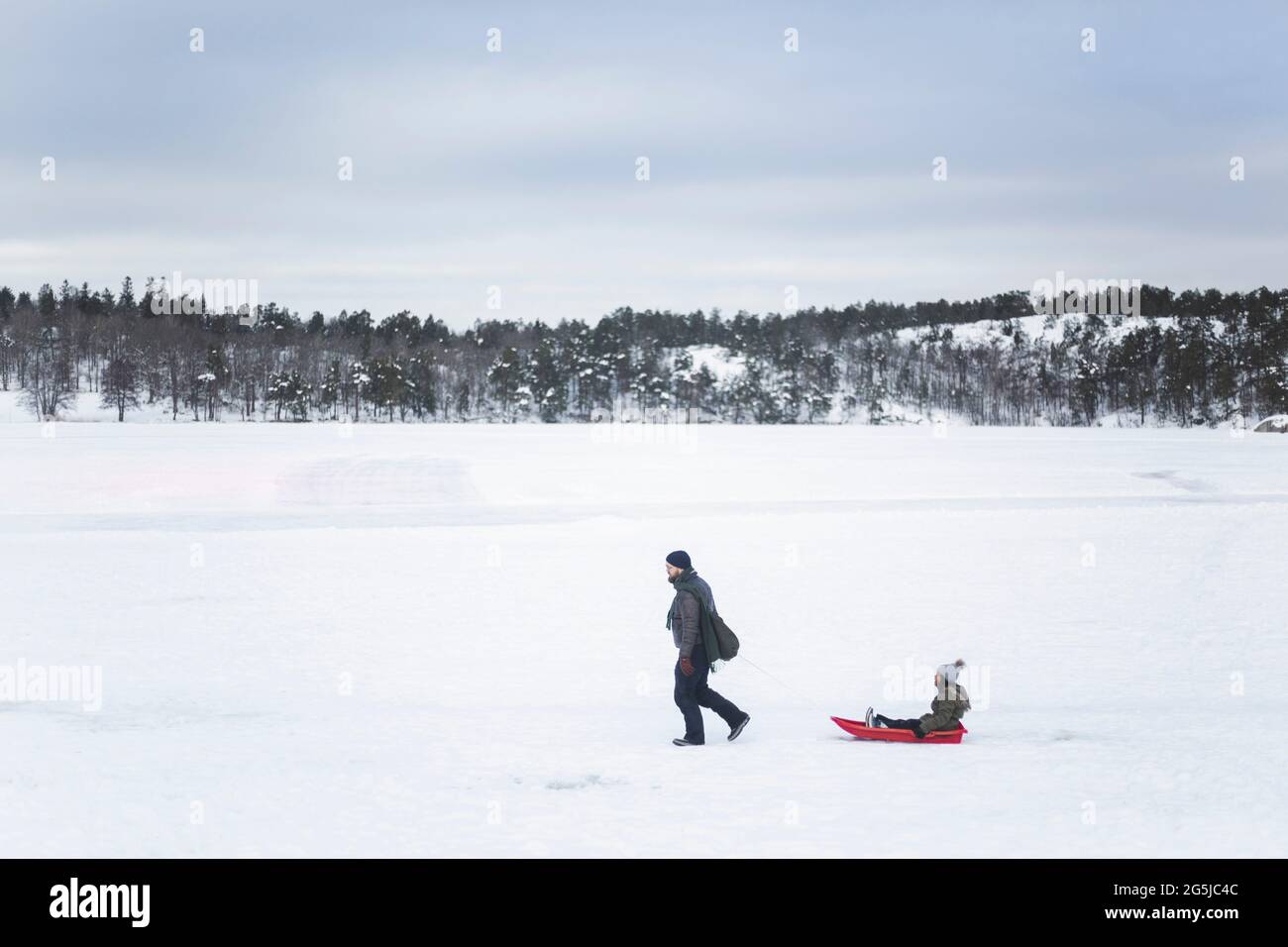 Pleine longueur d'homme tirant fille assis sur toboggan tout en marchant pendant l'hiver Banque D'Images