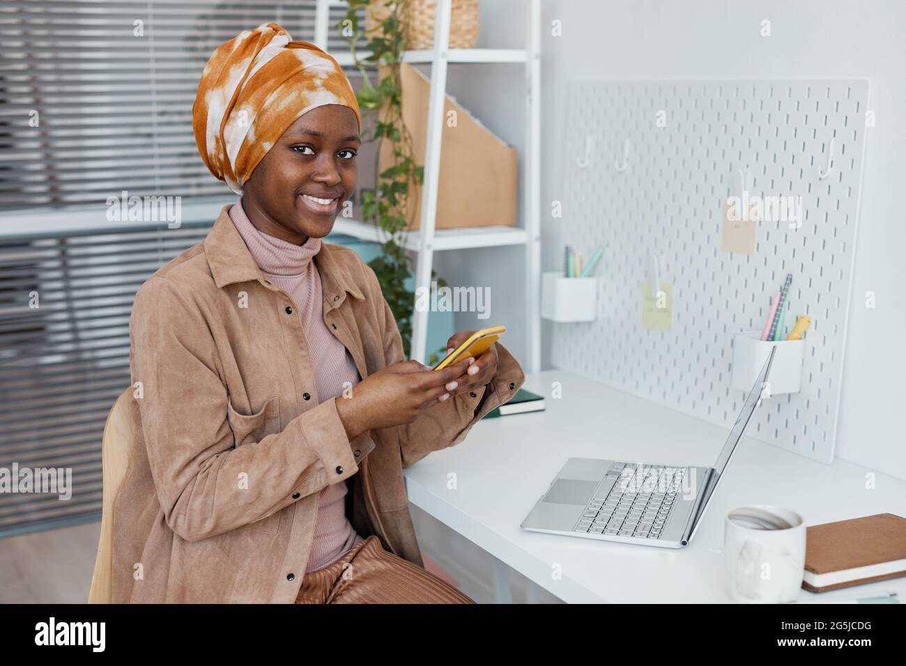 Portrait d'une femme afro-américaine moderne portant un foulard au bureau et souriant à l'appareil photo, espace de copie Banque D'Images