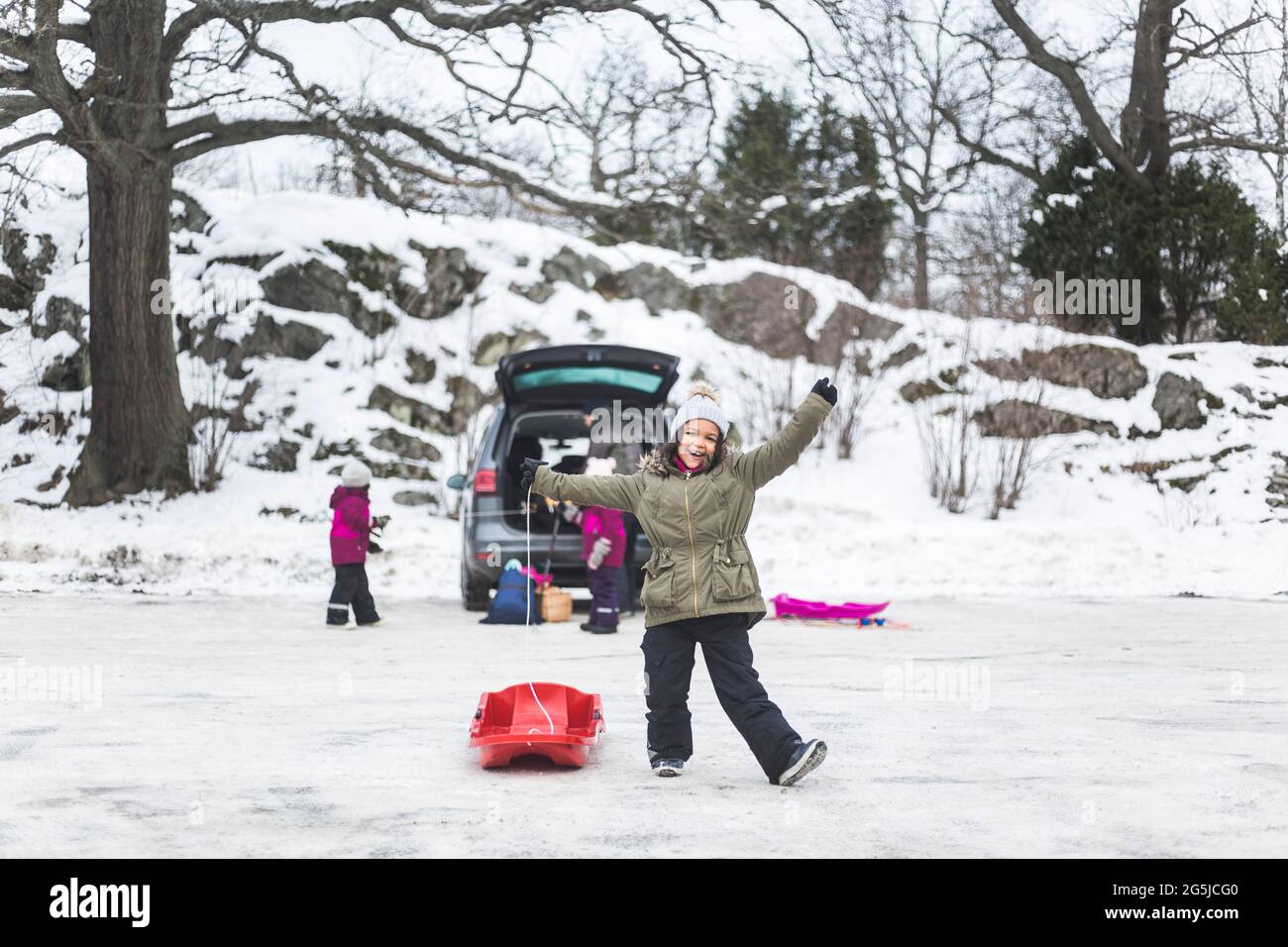 Pleine longueur de fille heureuse debout avec toboggan sur la neige contre la famille Banque D'Images