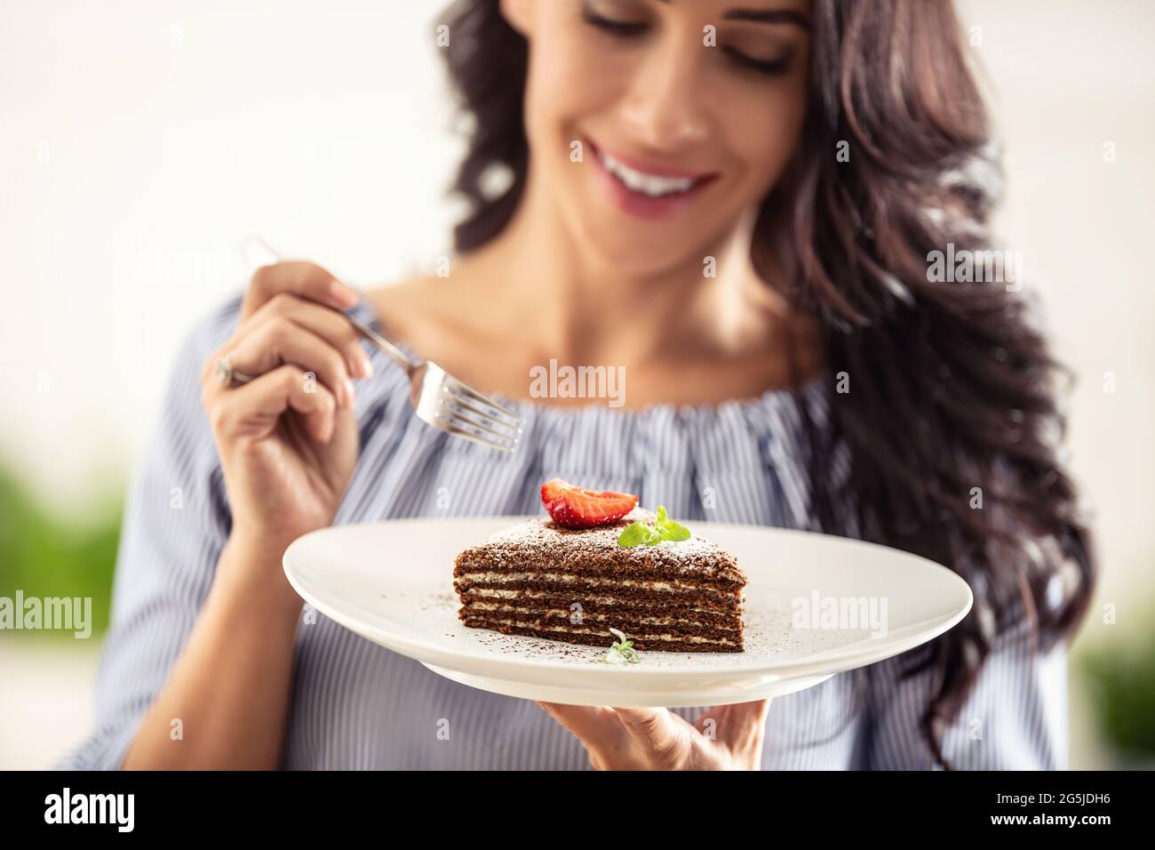 Gâteau blanc superposé brun adn avec feuille de fraise et de menthe sur le dessus tenu par une femme avec une fourchette. Banque D'Images