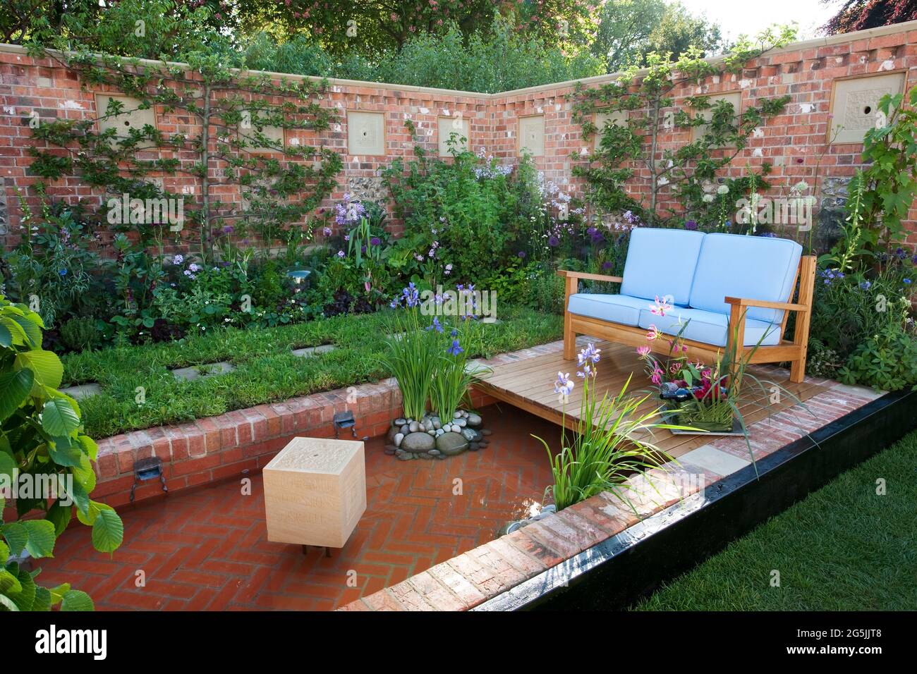 Canapé extérieur dans un petit jardin de cuisine clos, arbres fruitiers en espaliers, étang en brique formelle, boulettes d'abeilles dans le mur Banque D'Images