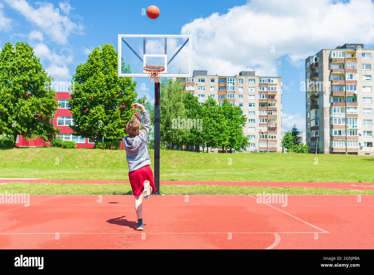 Joli petit garçon de tir balle au cerceau à l'aire de jeux.mignon jeune garçon joue au basket-ball sur l'aire de jeux en été chaud jour. Banque D'Images