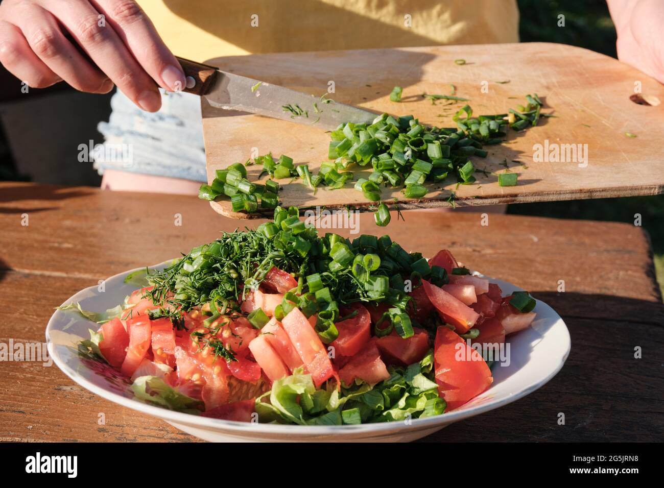 Fille ajoute des oignons à la salade de légumes. Cuisiner dans la nature. Banque D'Images