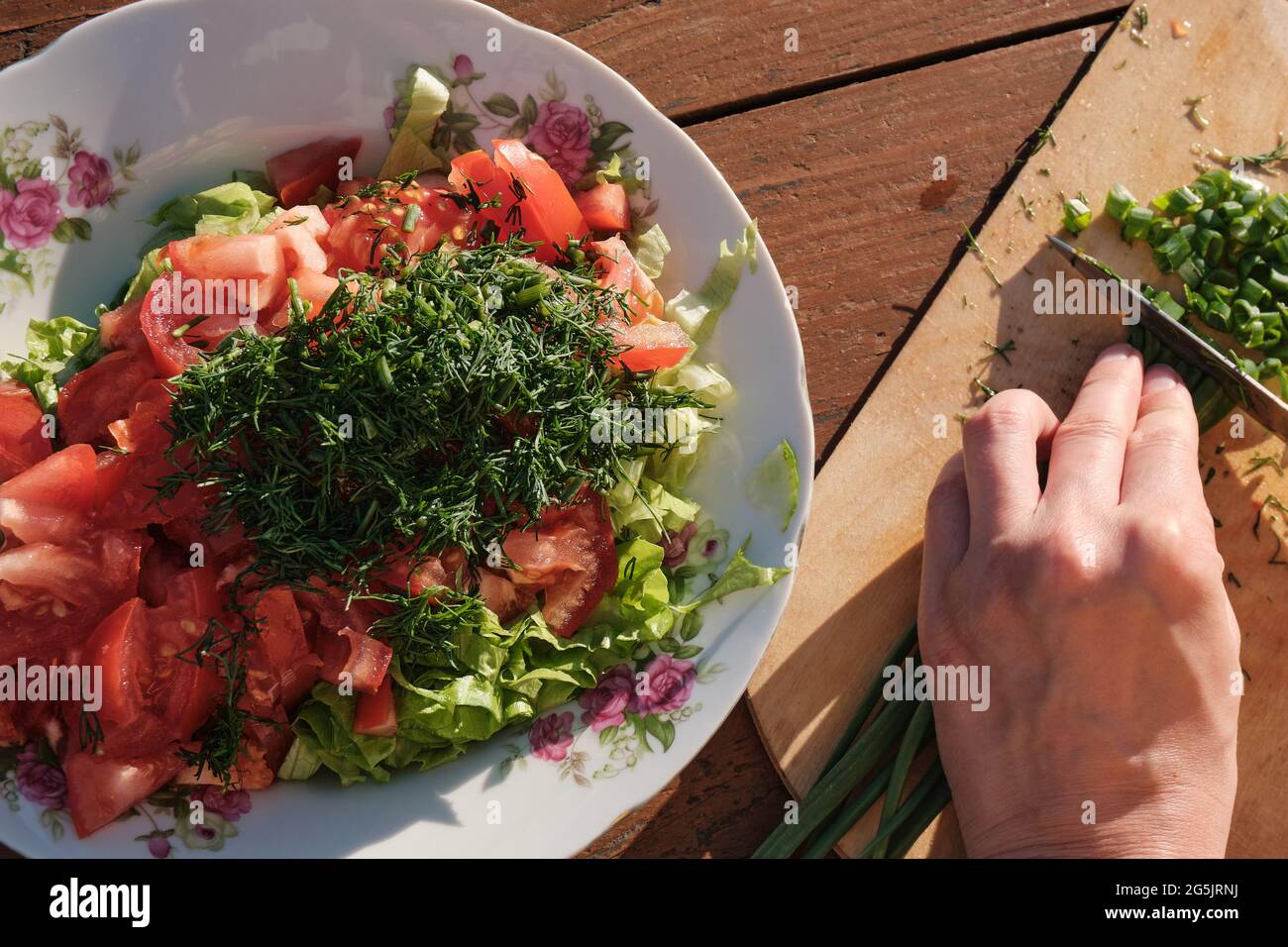 Une fille coupe l'oignon sur une planche en bois. Assiette de légumes. Cuisiner dans la nature. Banque D'Images