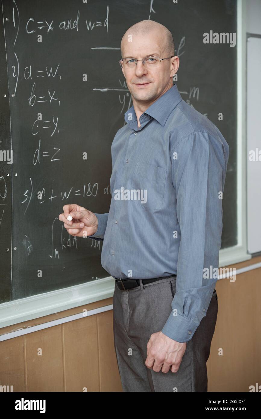 Professeur confiant debout au tableau noir avec des formules à la leçon Banque D'Images