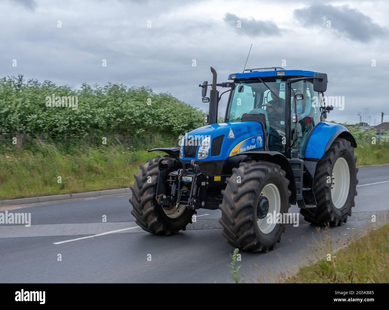 27 juin 2021 - Pocklington, East Yorkshire, Royaume-Uni - Beacon Young Farmers Club Tractor Run. Tracteur bleu sur route Tarmac avec haie. Banque D'Images