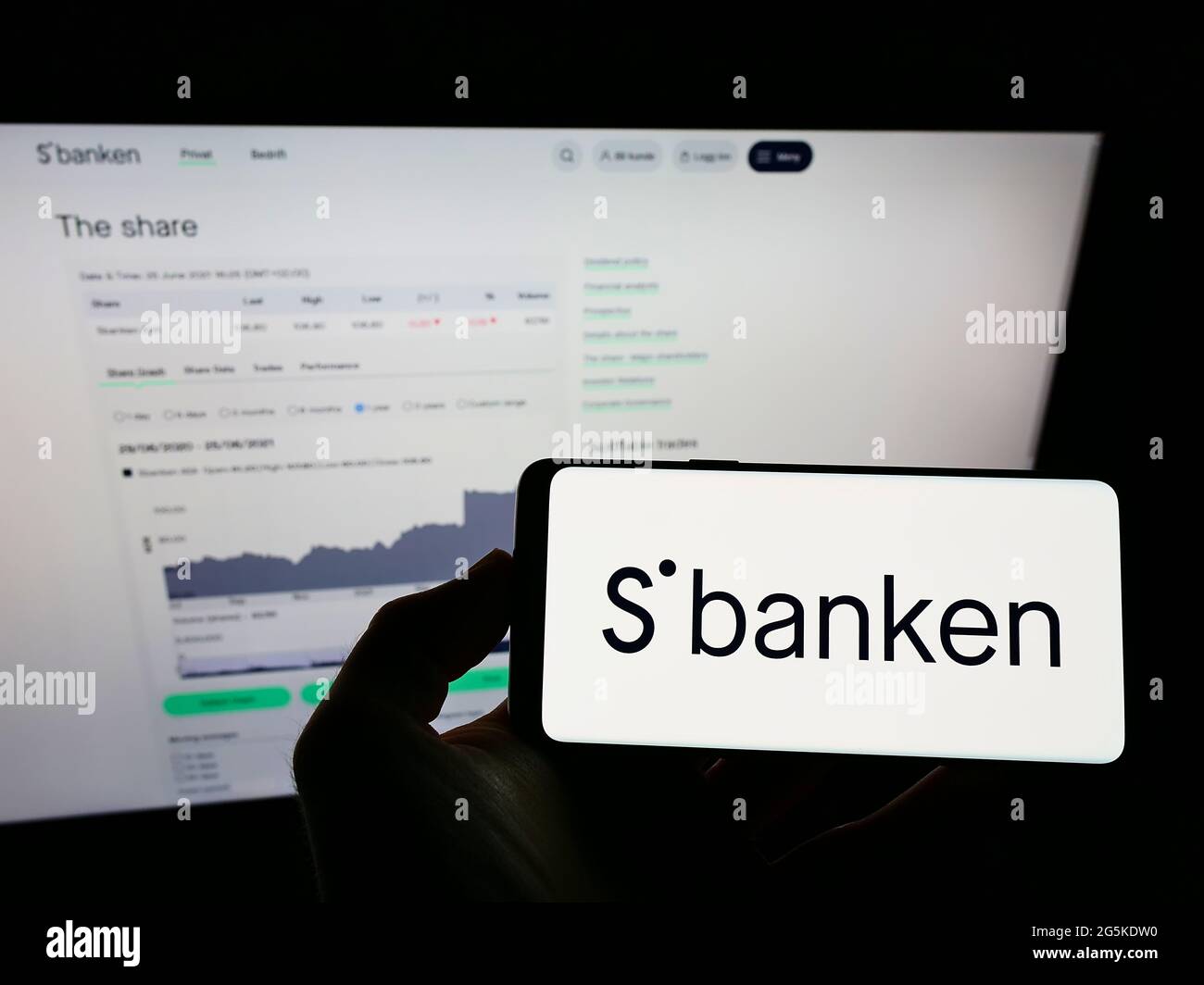 Personne tenant un téléphone portable avec le logo de la banque en ligne norvégienne Sbanken ASA à l'écran en face de la page web d'affaires. Mise au point sur l'affichage du téléphone. Banque D'Images