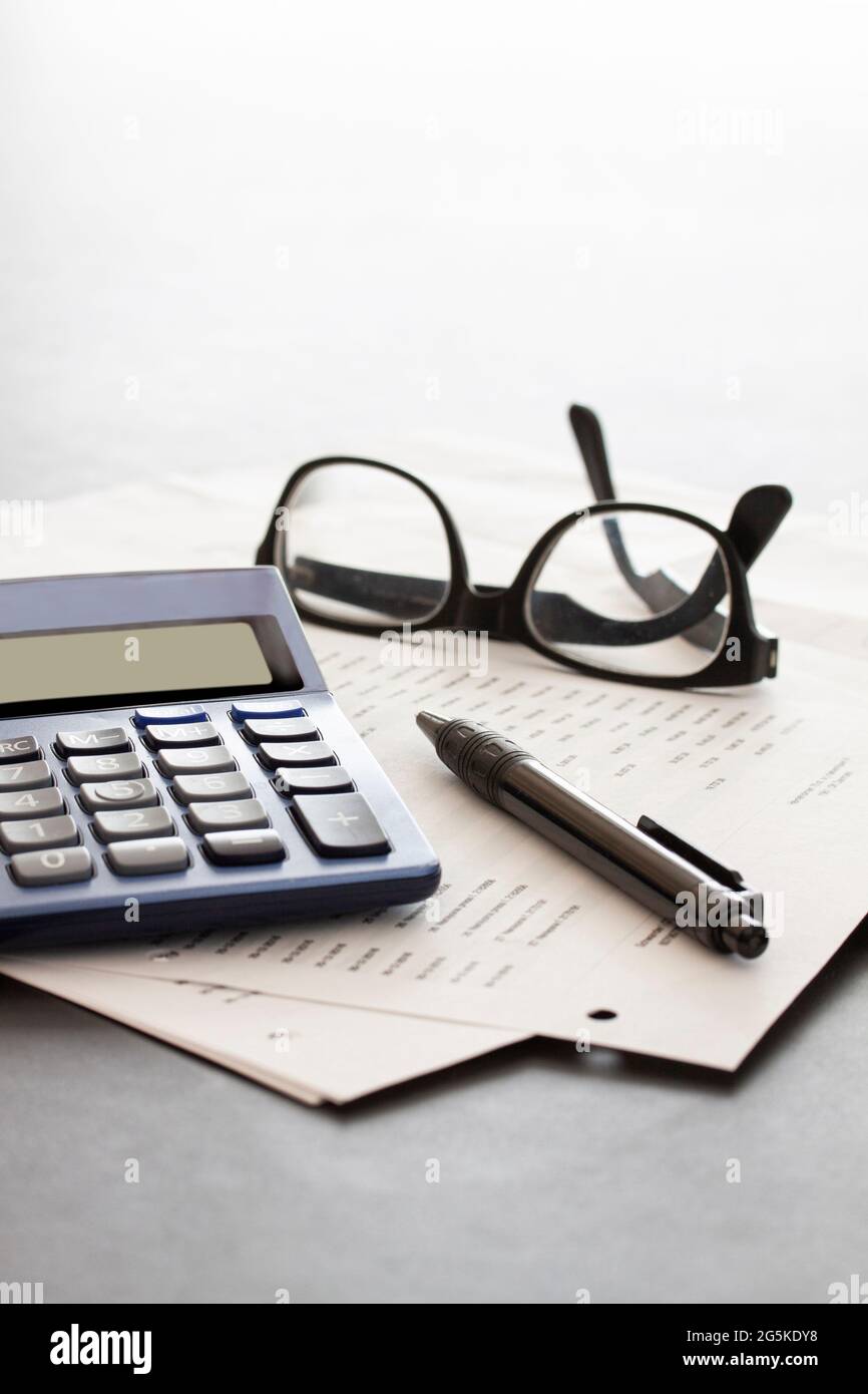 calculatrice, lunettes, stylo et papiers sur fond blanc fondu avec espace de copie. Concept d'entreprise. Banque D'Images
