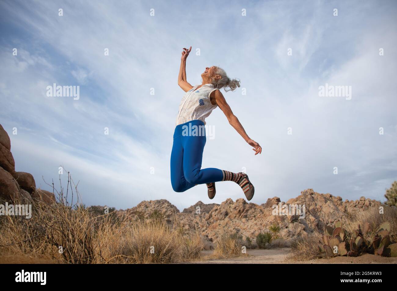 Femme âgée sautant volontiers dans un désert. Banque D'Images