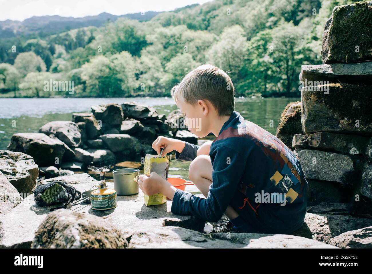 Garçon cuisinant à l'extérieur en campant à côté d'un lac au pays de Galles, au Royaume-Uni Banque D'Images