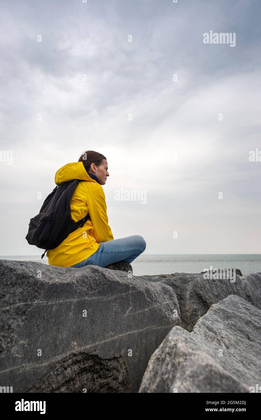 Femme routard portant une veste jaune assise sur des rochers qui donnent sur la mer. S'éloigner de tout. Banque D'Images