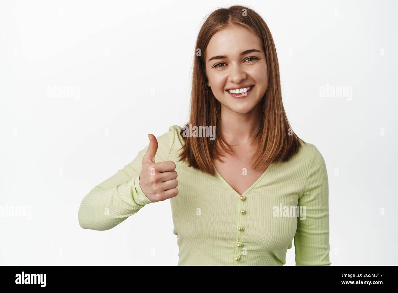 Très bien. Une jeune femme souriante se montre au pouce vers le haut dans l'approbation, garantie de qualité, recommander un endroit ou un produit, comme et d'accord, commentaires positifs, debout Banque D'Images