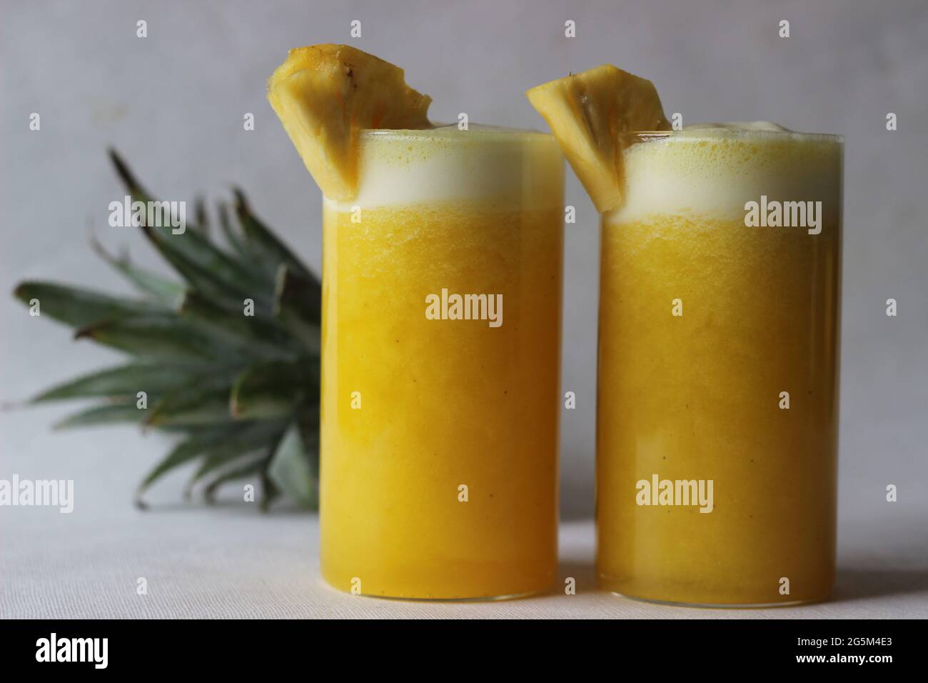Jus d'ananas frais pour battre la chaleur estivale. Jus fait maison servi dans un long verre décoré d'un coin d'ananas. Prise de vue sur fond blanc Banque D'Images