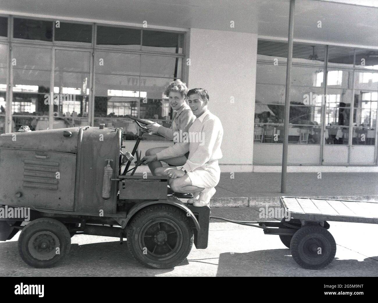 1957, historique, camp de vacances de Prestatyn, à l'extérieur de la salle à manger, un couple de vacances assis sur un petit véhicule utilitaire de camp avec remorque. Le centre de vacances de Prestatyn, pays de Galles, a été construit par la London Midland and Scottish Railway Co. En 1939, avec les principaux bâtiments dans le style de 1930s, avec des extrémités de bâtiment arrondies et des fenêtres encadrées d'acier. Banque D'Images