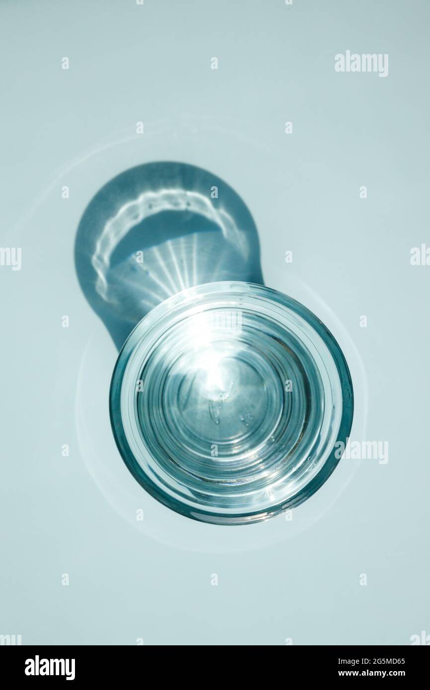 Un verre d'eau claire, disposition minimale, réflexion de lumière, jeu d'ombre. Fond bleu pastel Banque D'Images