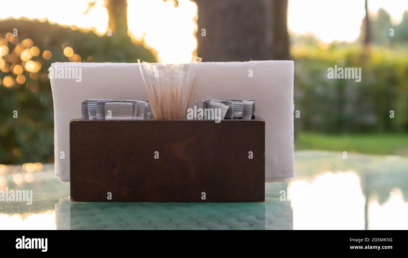 Un porte-serviette en bois marron et des cure-dents sont installés sur la table en verre du café, illuminés par les rayons du soleil. Table dans le restaurant. Verre Banque D'Images