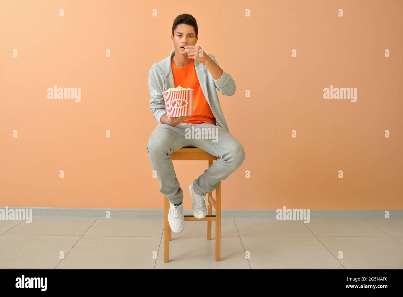 Adolescent afro-américain qui mange du pop-corn près du mur de couleur Banque D'Images