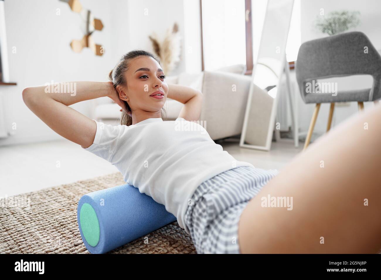 Jeune femme faisant de l'exercice avec le rouleau de gymnastique sur le sol à la maison Banque D'Images