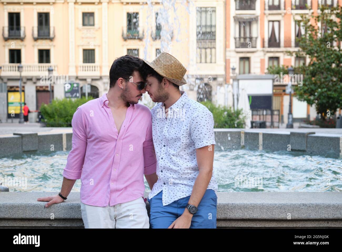Jeune couple gay ayant un moment d'affection à la fontaine dans une place de la ville. Banque D'Images