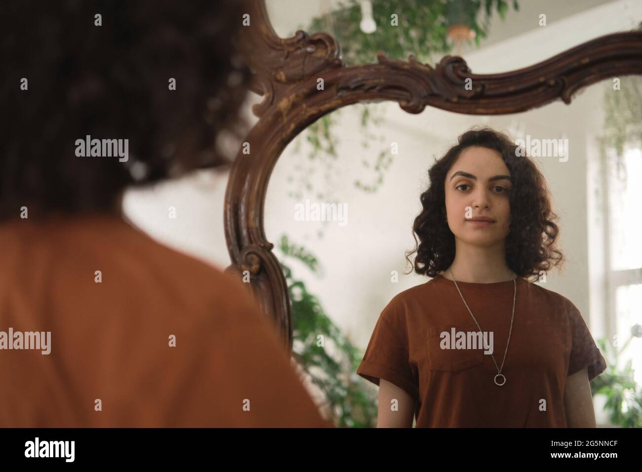 Jeune femme aux cheveux bouclés debout devant le miroir et regardant elle-même Banque D'Images