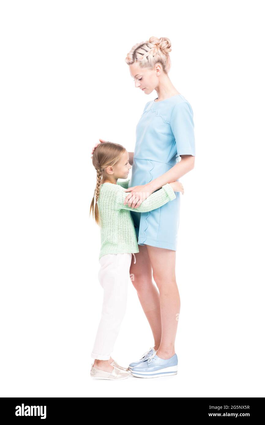 Coupe verticale pleine de petite fille mignonne avec deux tresses embrassant sa mère aimante, fond blanc Banque D'Images