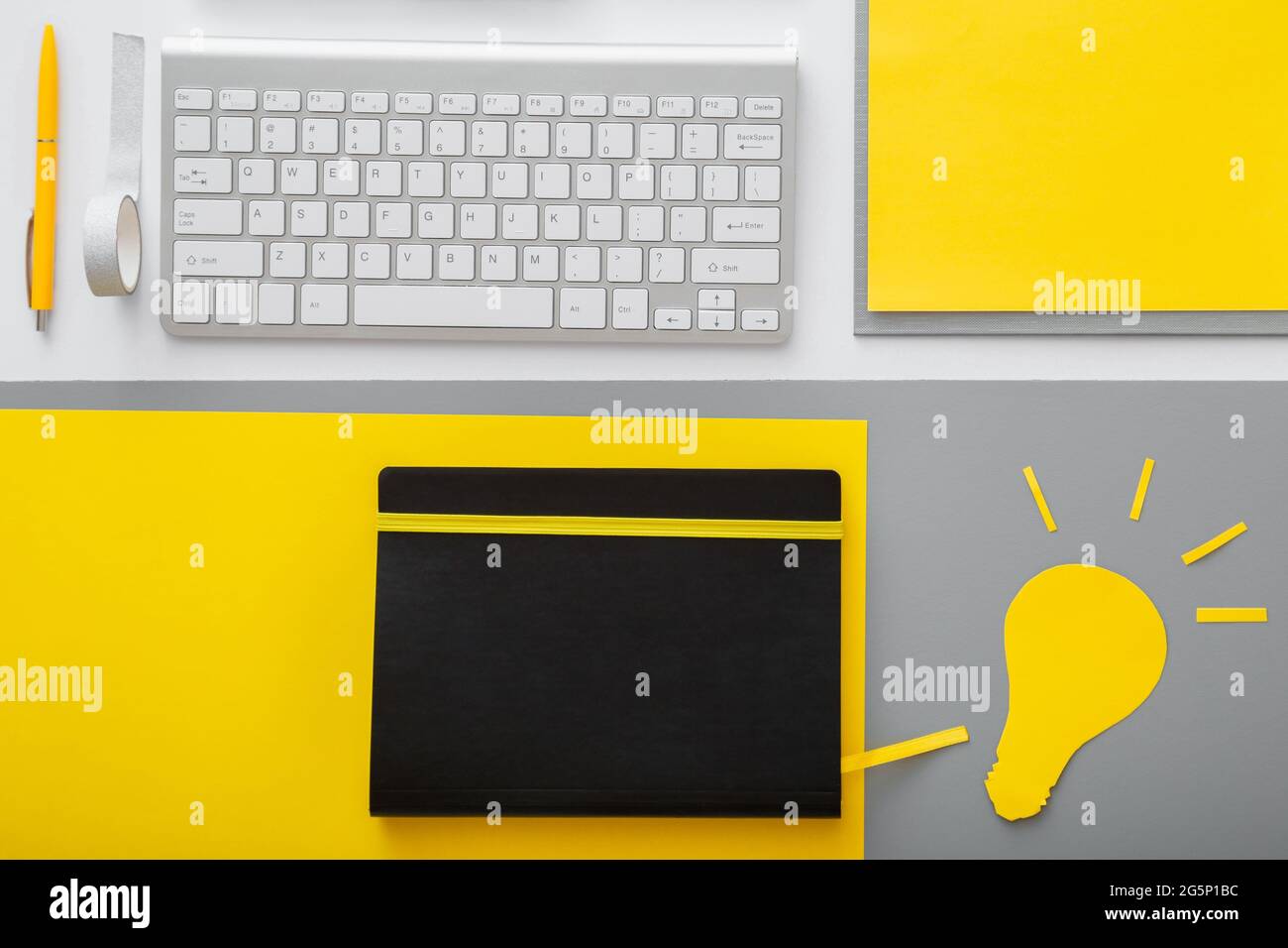 Métaphore de l'idée de l'ampoule jaune sur le bureau avec clavier pc ordinateur et fournisseurs dans l'espace de travail sur fond de table gris. Banque D'Images