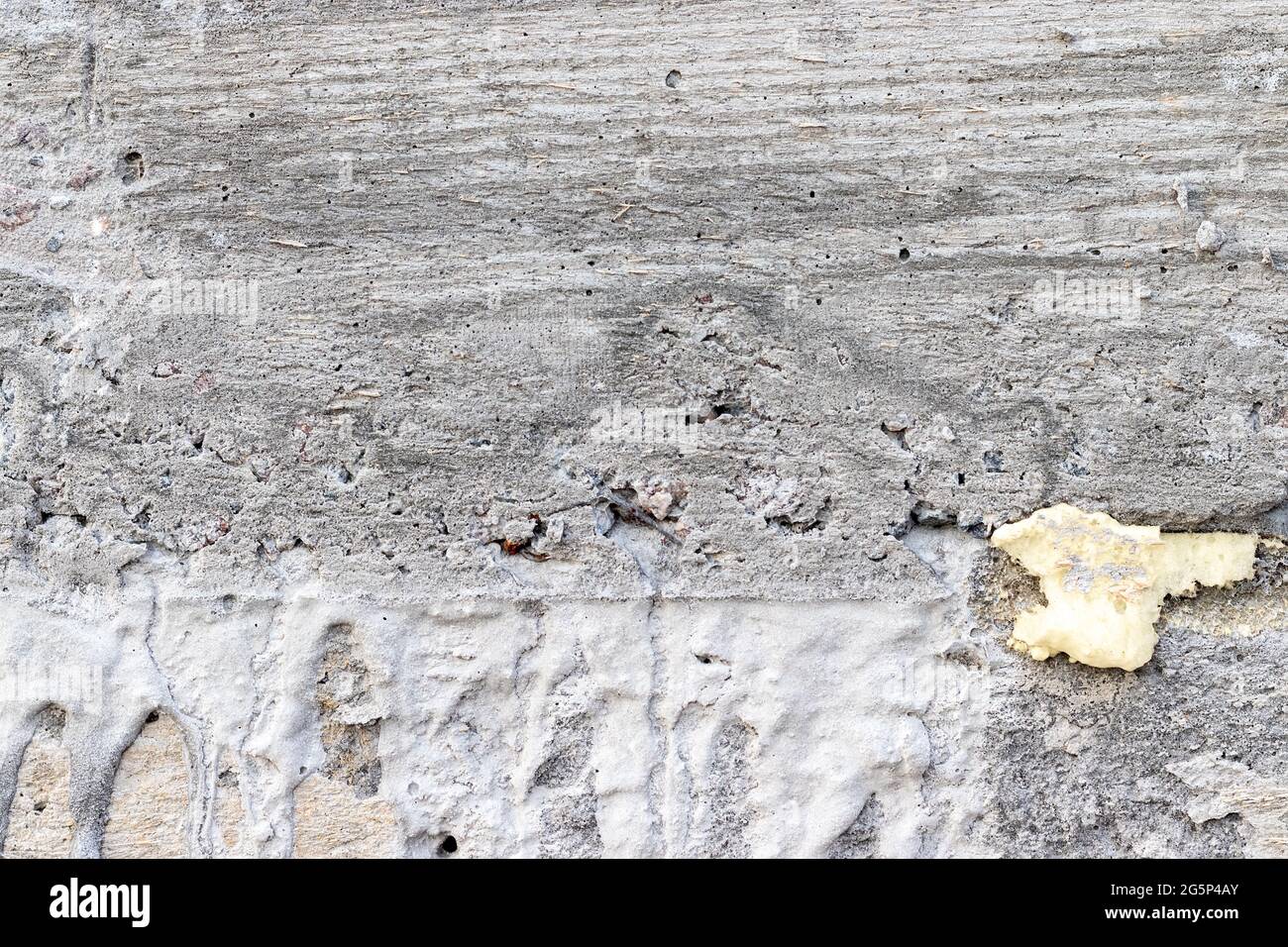 Texture d'arrière-plan grise, rugueuse, en béton. Mur avec trous, diverses éclaboussures et mousse de polyuréthane jaune Banque D'Images