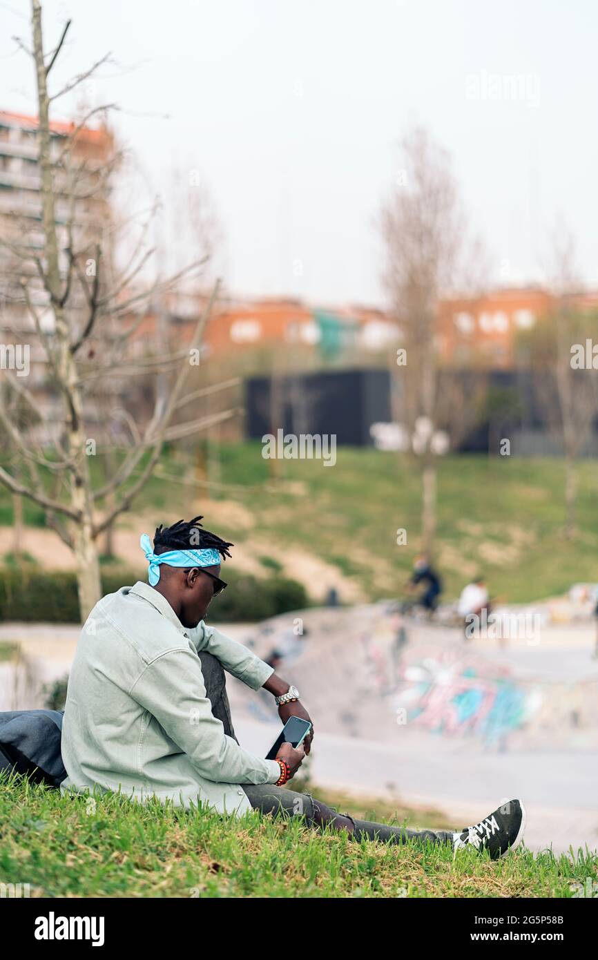 Jeune homme africain assis dans l'herbe et en utilisant son téléphone portable. Banque D'Images