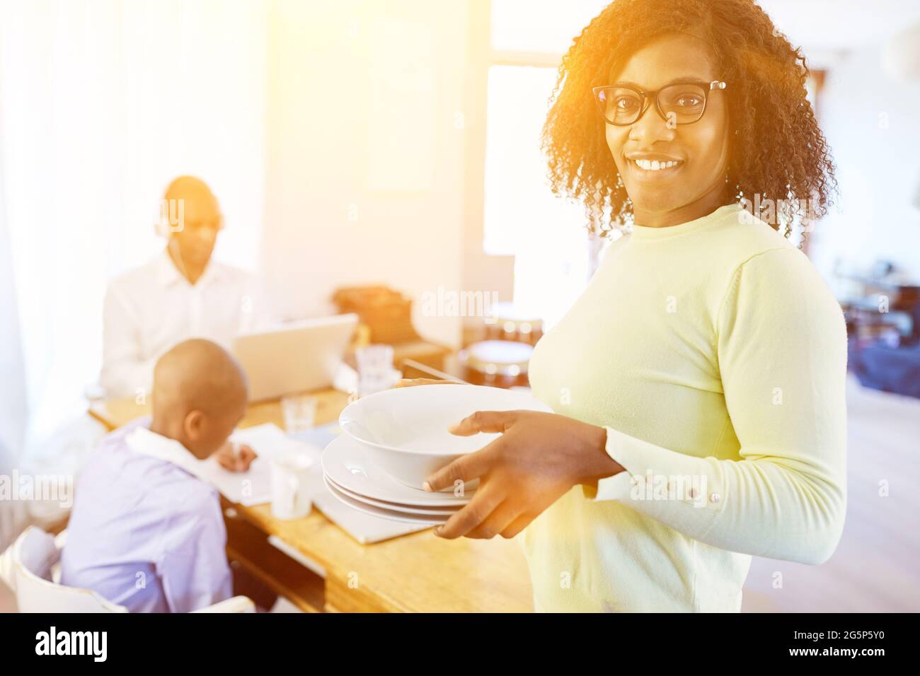 Famille afro-américaine dans le bureau à domicile avec homeschooling et femme portant des plats dans la vie quotidienne Banque D'Images