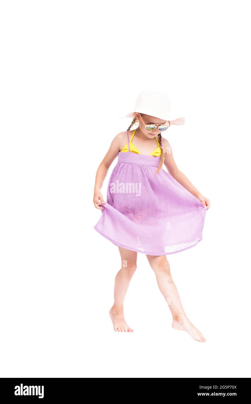 Portrait de studio vertical de petite fille caucasienne portant une robe d'été, des lunettes de soleil et un chapeau posé sur l'appareil photo, fond blanc Banque D'Images