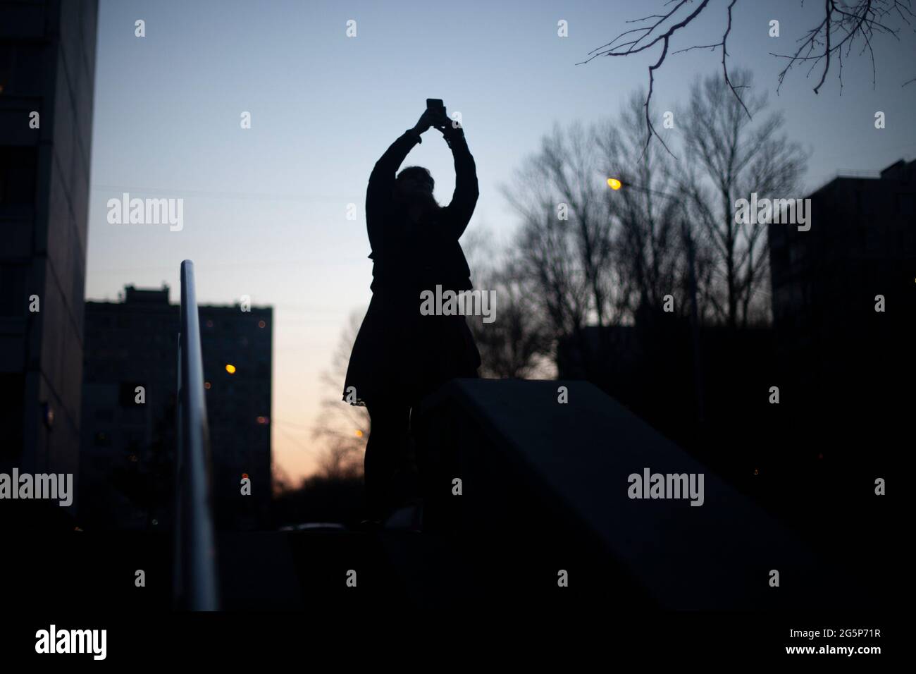 La silhouette d'une fille prenant une photo du ciel de la soirée. Une fille marche la nuit dans la rue. Banque D'Images