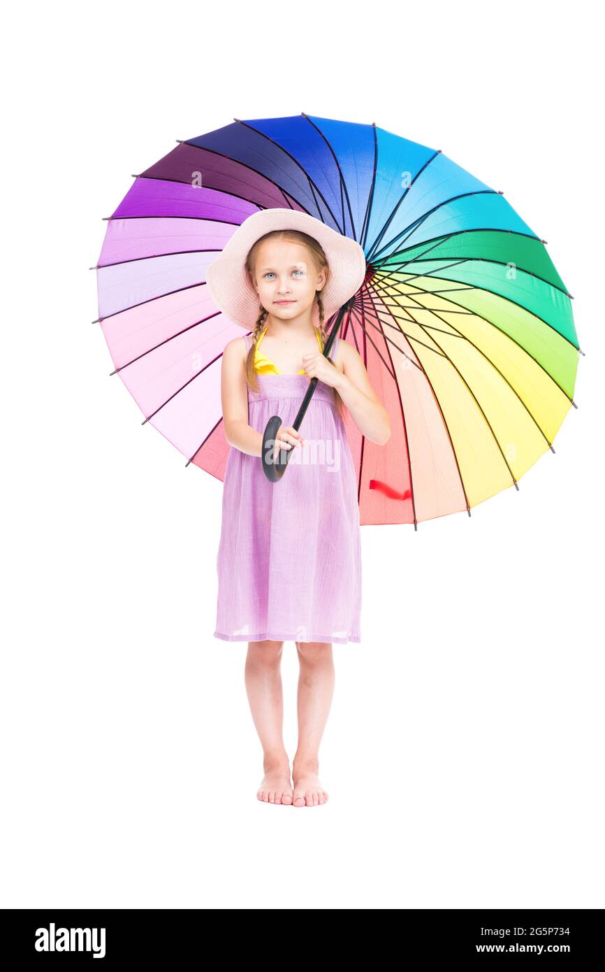 Portrait de studio vertical de petite fille caucasienne portant une robe d'été et un chapeau tenant un parapluie coloré posé sur l'appareil photo, fond blanc Banque D'Images