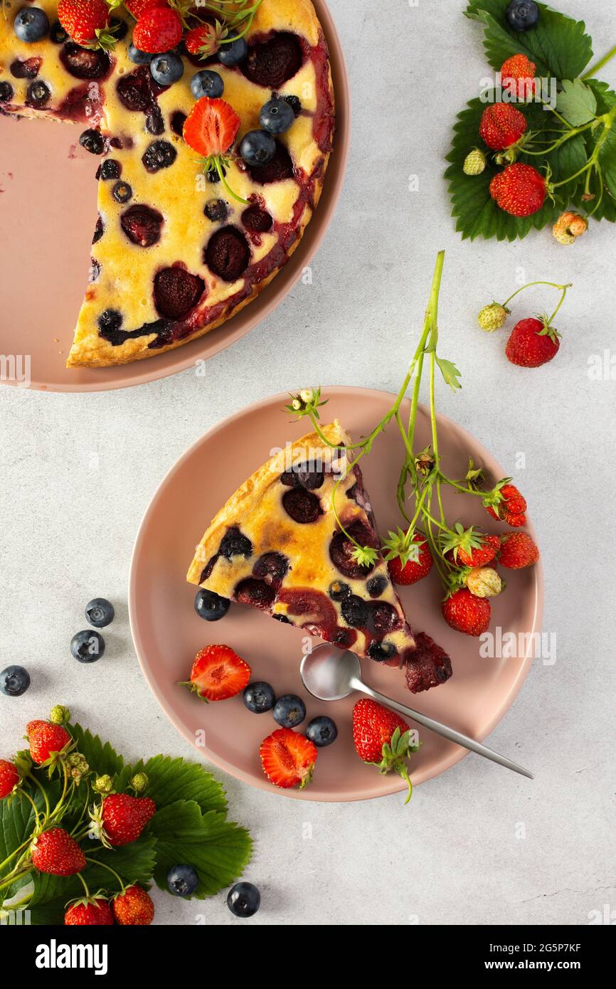 Morceau de tarte aux fraises et aux myrtilles avec baies fraîches dans une assiette rose sur fond gris, vue du dessus Banque D'Images
