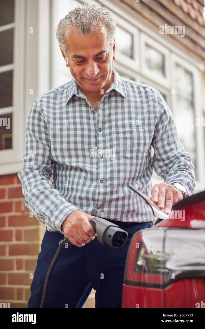 Homme mature qui attache le câble de chargement à une voiture électrique écologique sans émission à la maison Banque D'Images