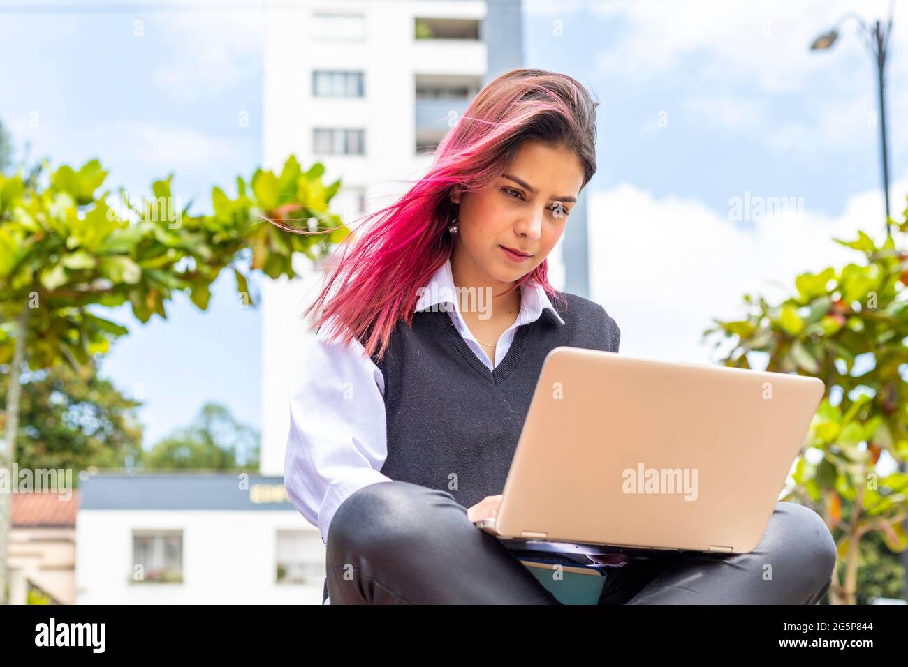 Jeune et belle femme hispanique utilisant son PC portable tout en étant assise sur la paillasse à l'extérieur. Banque D'Images