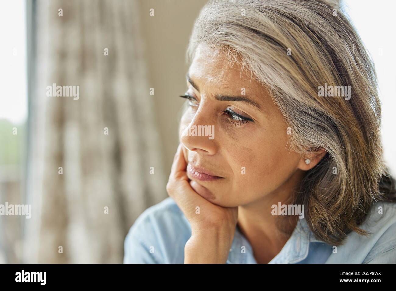 Tête et épaules prise de vue d'une femme mûre réfléchie regardant hors de la fenêtre à la maison Banque D'Images
