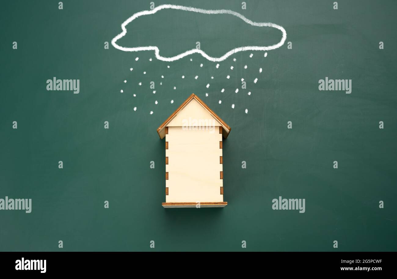 une maison en bois et un nuage dessiné avec de la pluie avec de la craie blanche sur un tableau de craie vert. Concept d'assurance immobilière Banque D'Images