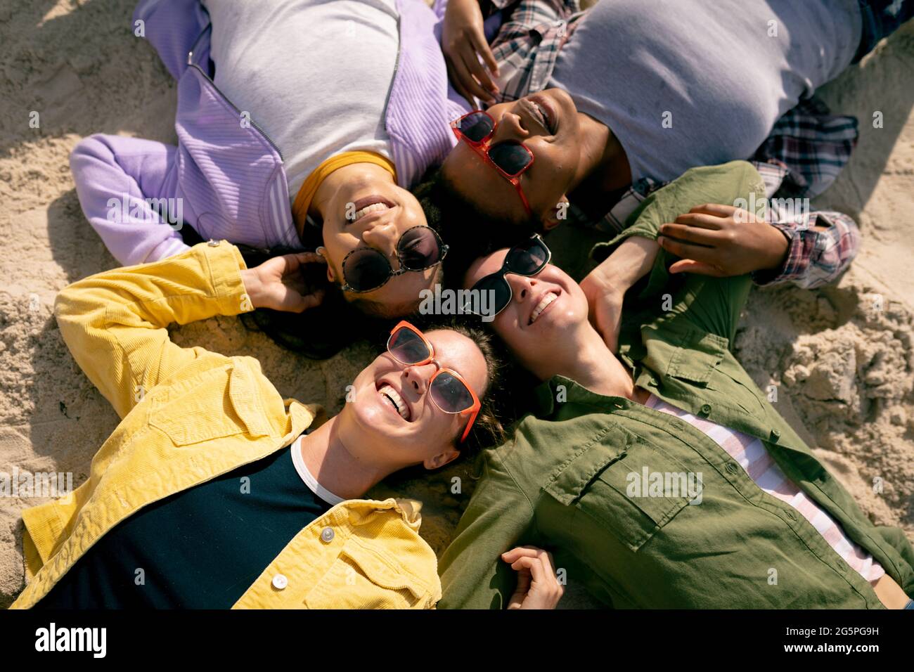 Groupe heureux de diverses amies féminines s'amuser, se poser sur la plage en tenant les mains et en riant Banque D'Images