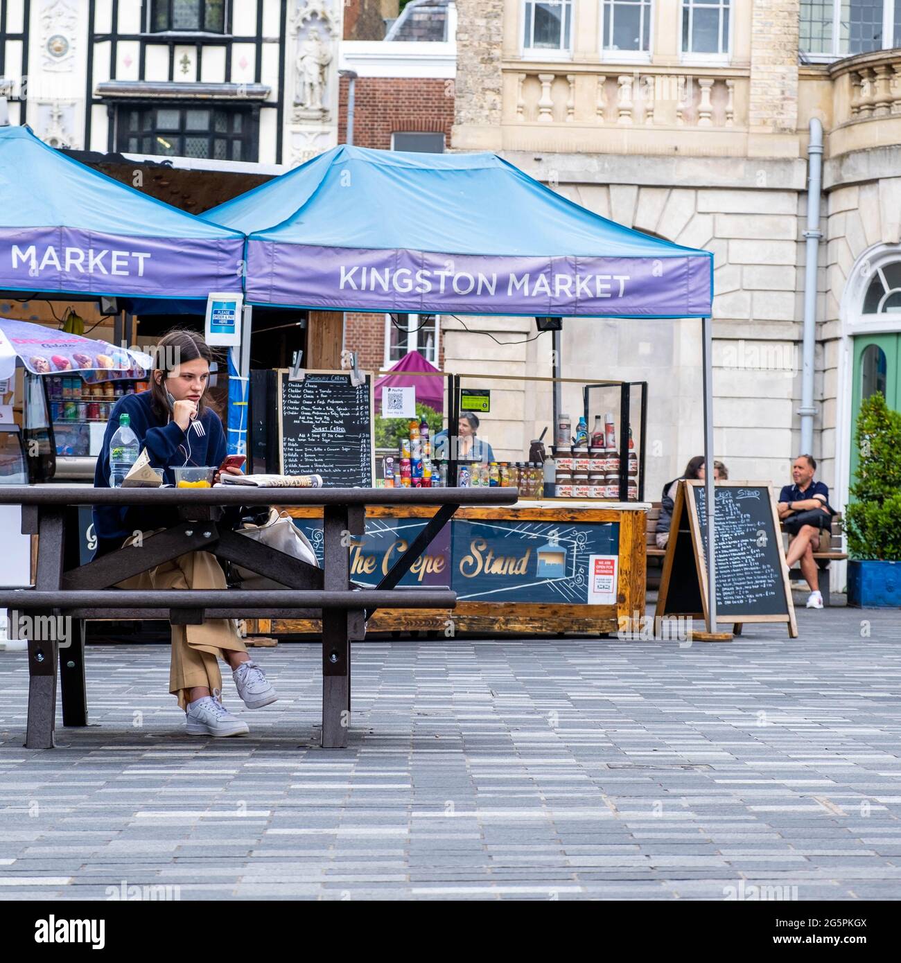 Kingston Londres UK, juin 29 2021, jeune femme assise seule à l'extérieur sur un banc en bois manger UN repas ou un déjeuner à emporter Banque D'Images