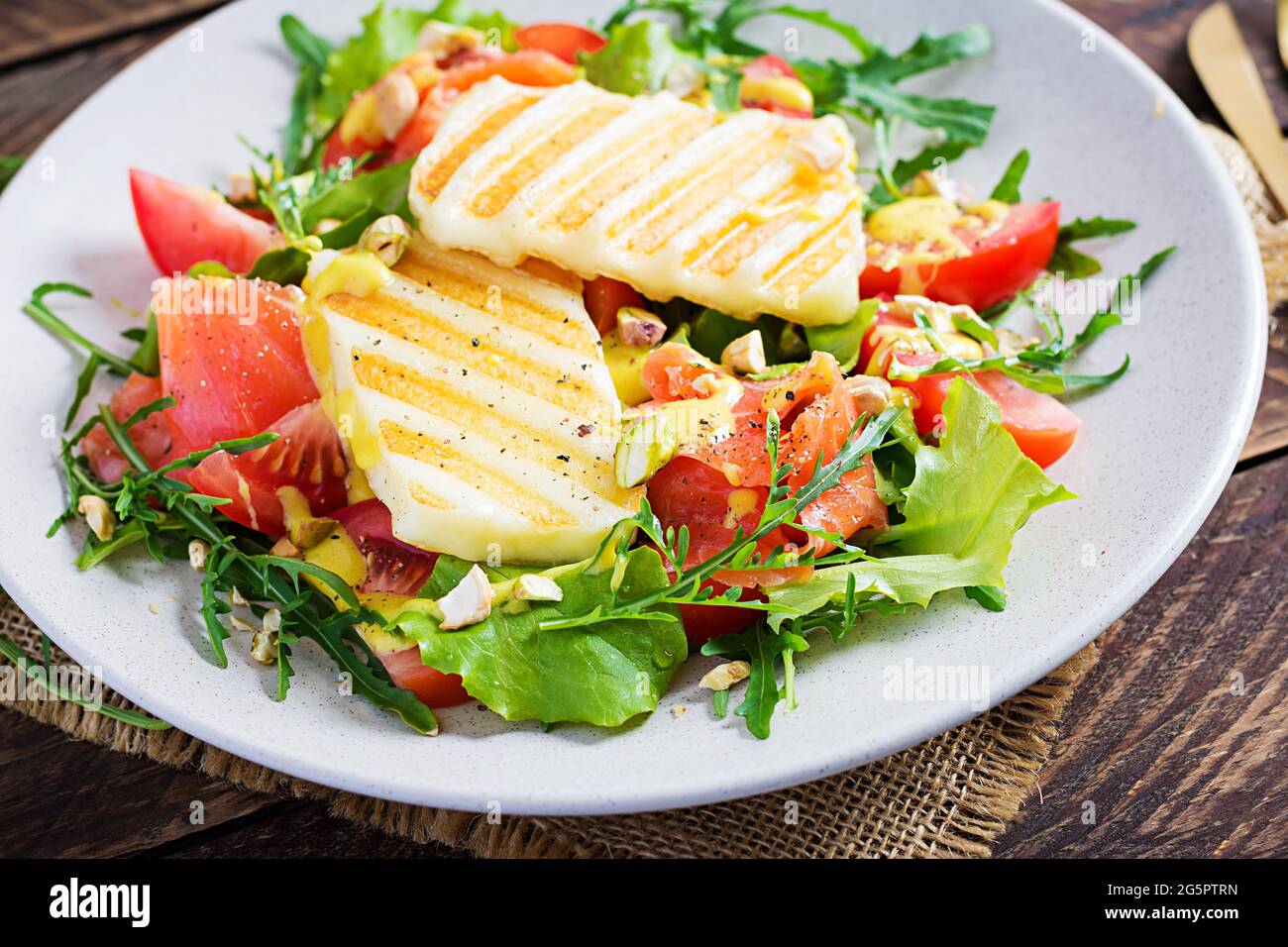 Salade de fromage halloumi grillé au saumon salé, aux tomates et aux herbes vertes. Nourriture saine sur plaque sur fond de bois. Banque D'Images