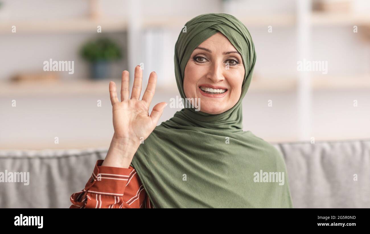 Bonne dame musulmane mature dans hijab en agitant la main à la maison Banque D'Images