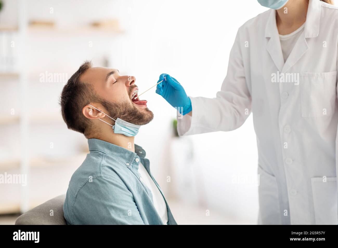 Médecin effectuant un test PCR du coronavirus oral chez le jeune homme à la clinique. Homme millénaire subissant une procédure de diagnostic de covid Banque D'Images