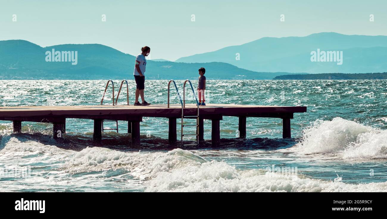 Urla, İzmir, Turquie - juin 2021 : un père parle à son fils sur un ponton en bois au-dessus de la mer à Urla, İzmir, Turquie. Banque D'Images