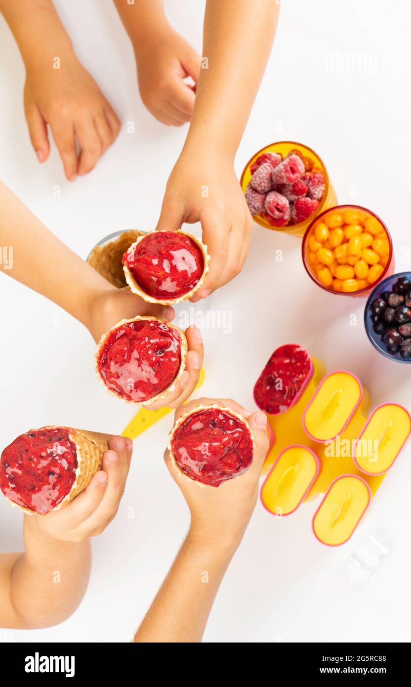 les enfants tiennent une cuillère de glace aux baies maison dans un cône de gaufres sur une table blanche. Dessert sain d'été nourriture végétarienne Banque D'Images