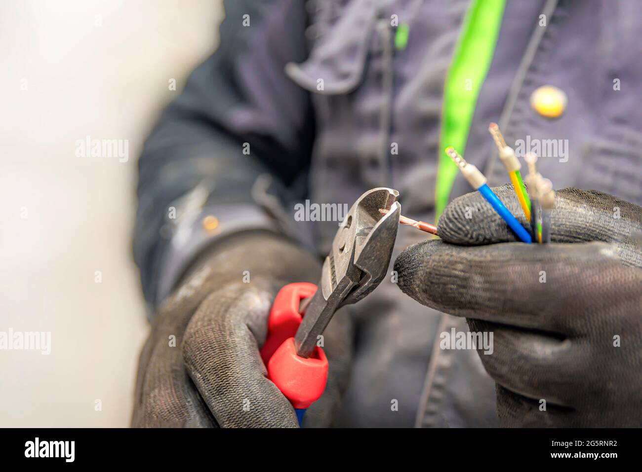 Les mains d'électricien tiennent les coupe-fils et les fils en gros plan. L'idée de réparer et de connecter le câblage électrique à la maison ou au travail Banque D'Images